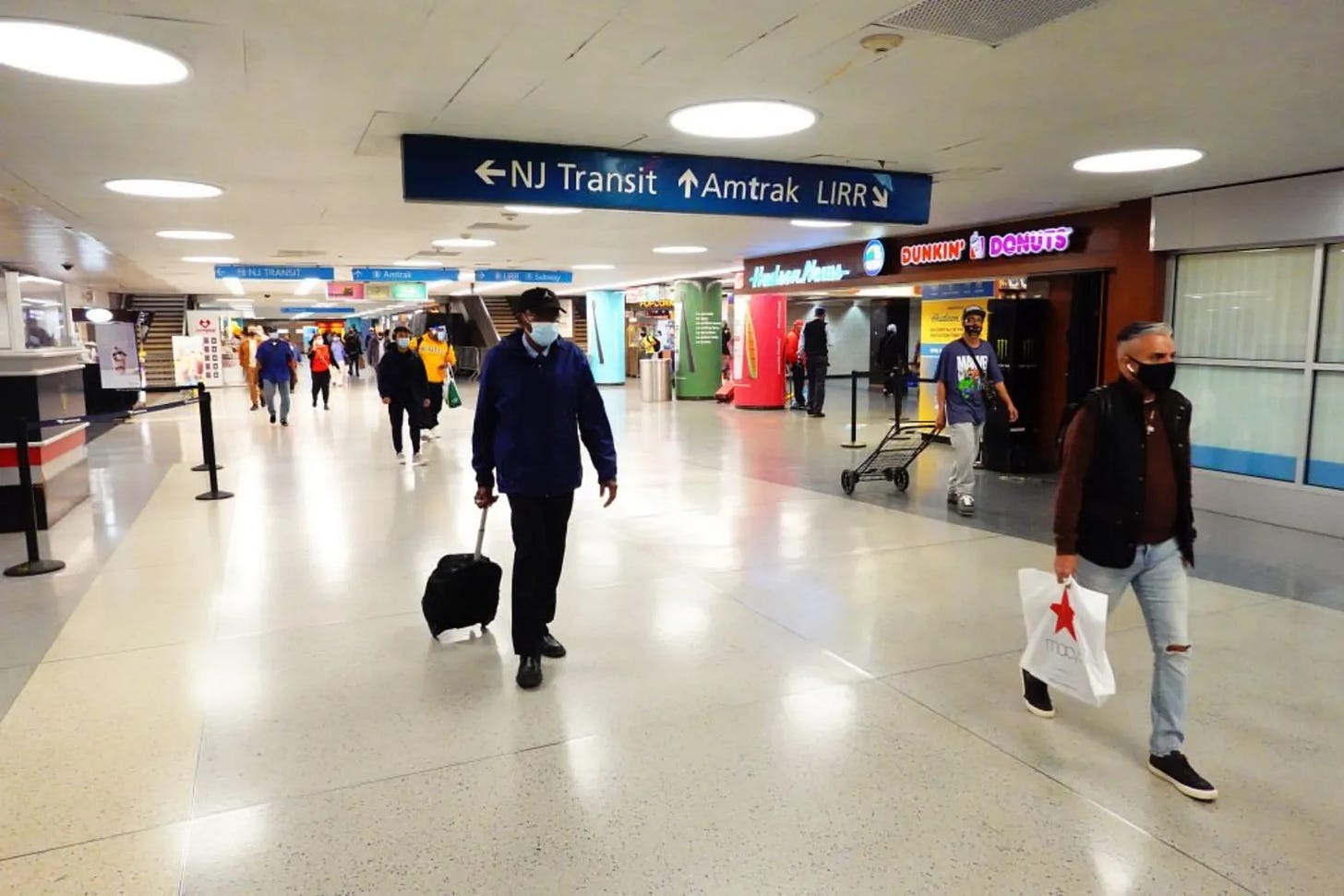 Inside Penn Station, including a Dunkin Donuts, Hudson News, and people walking with suitcases