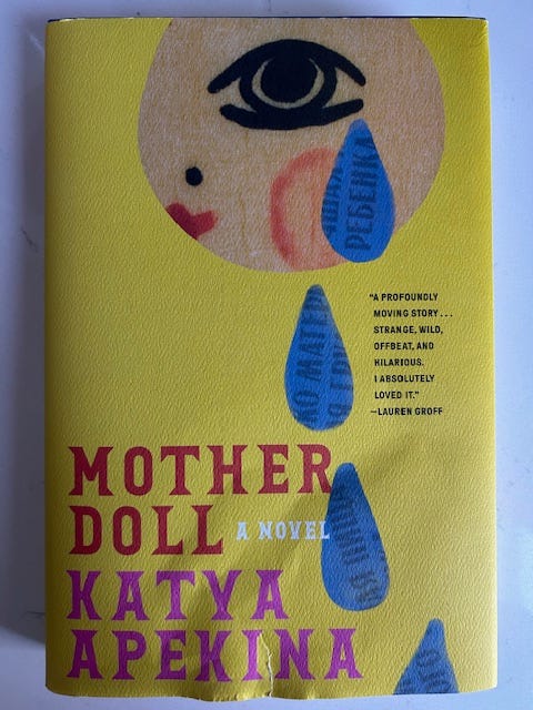 A yellow book cover has a drawing of an eye with blue tears falling from it. The text reads Mother Doll a Novel Katya Apekina