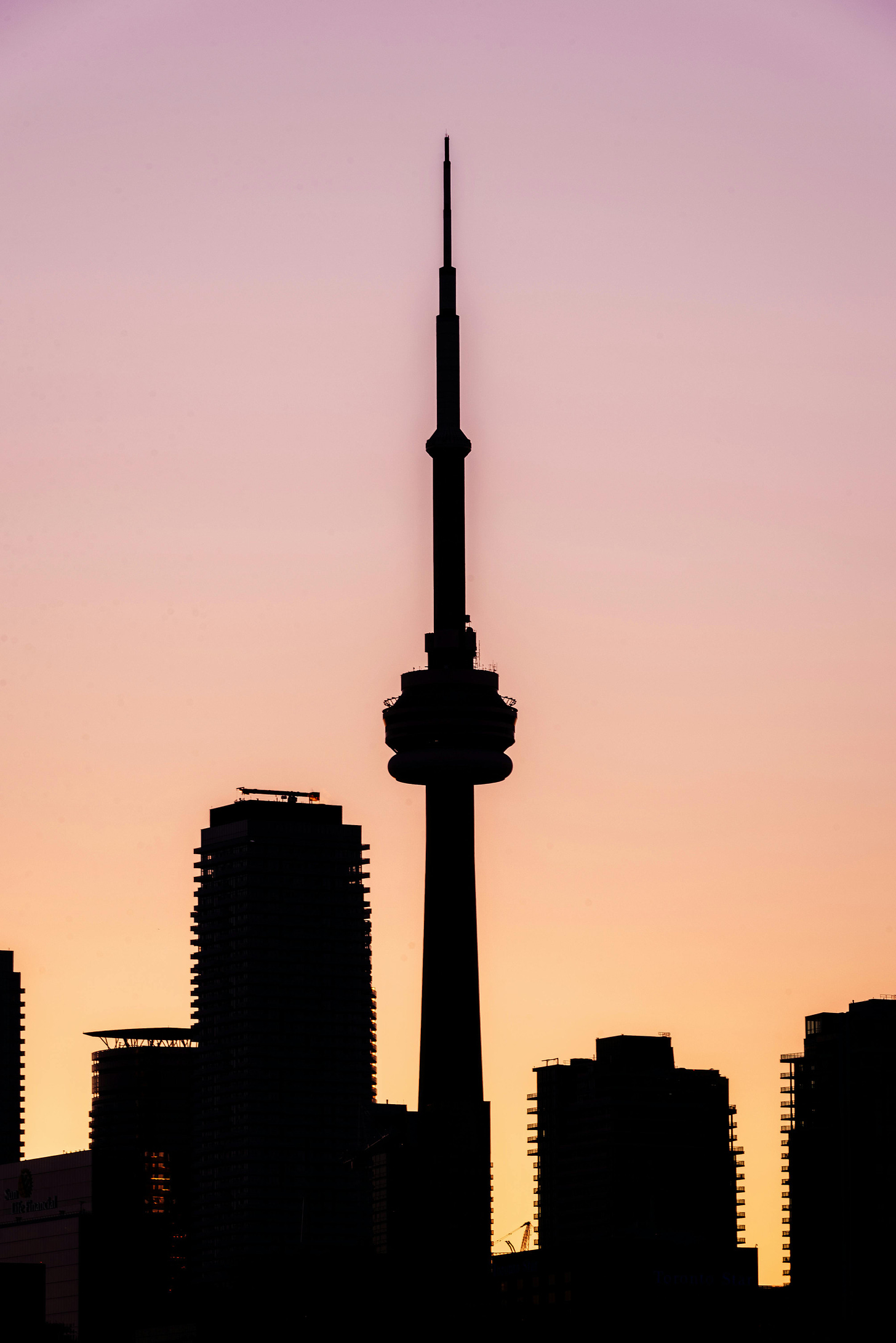 Silhouette of CN tower and buildings at dusk, pink sky.