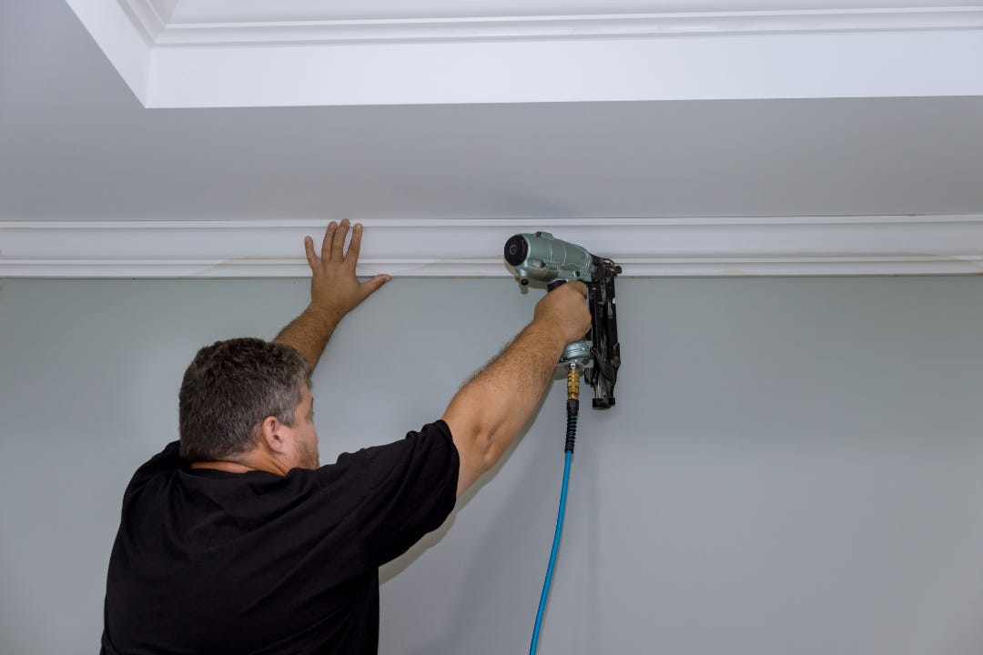 man installing crown molding, decorative wood trim along ceiling of a room