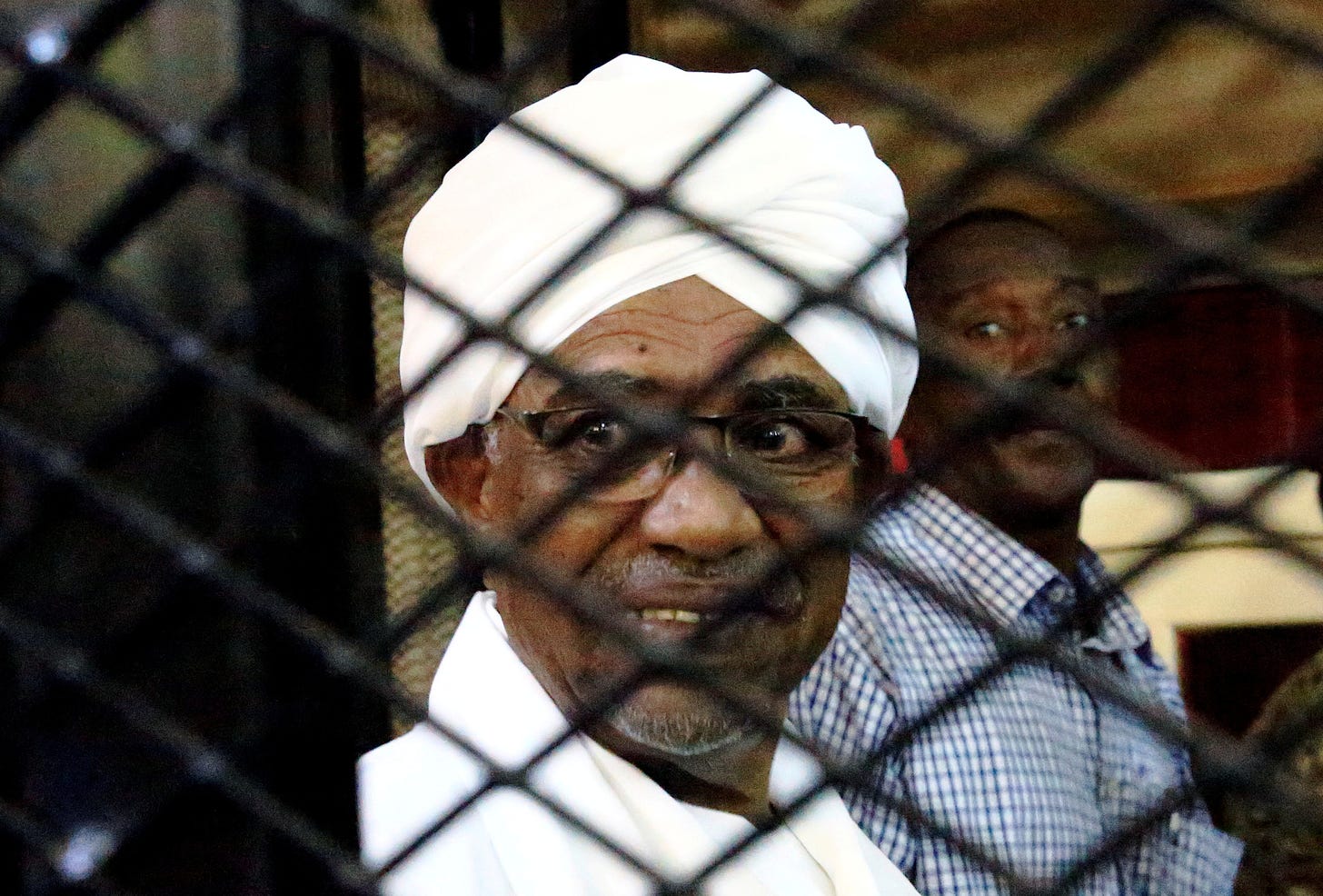 Sudan's former president Omar Hassan al-Bashir smiles as he is seen inside a cage at the courthouse where he is facing corruption charges, in Khartoum