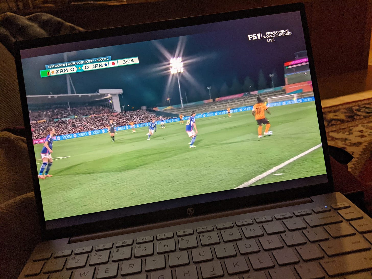 Laptop computer in a dark room showing Zambia vs. Japan in the Women's World Cup