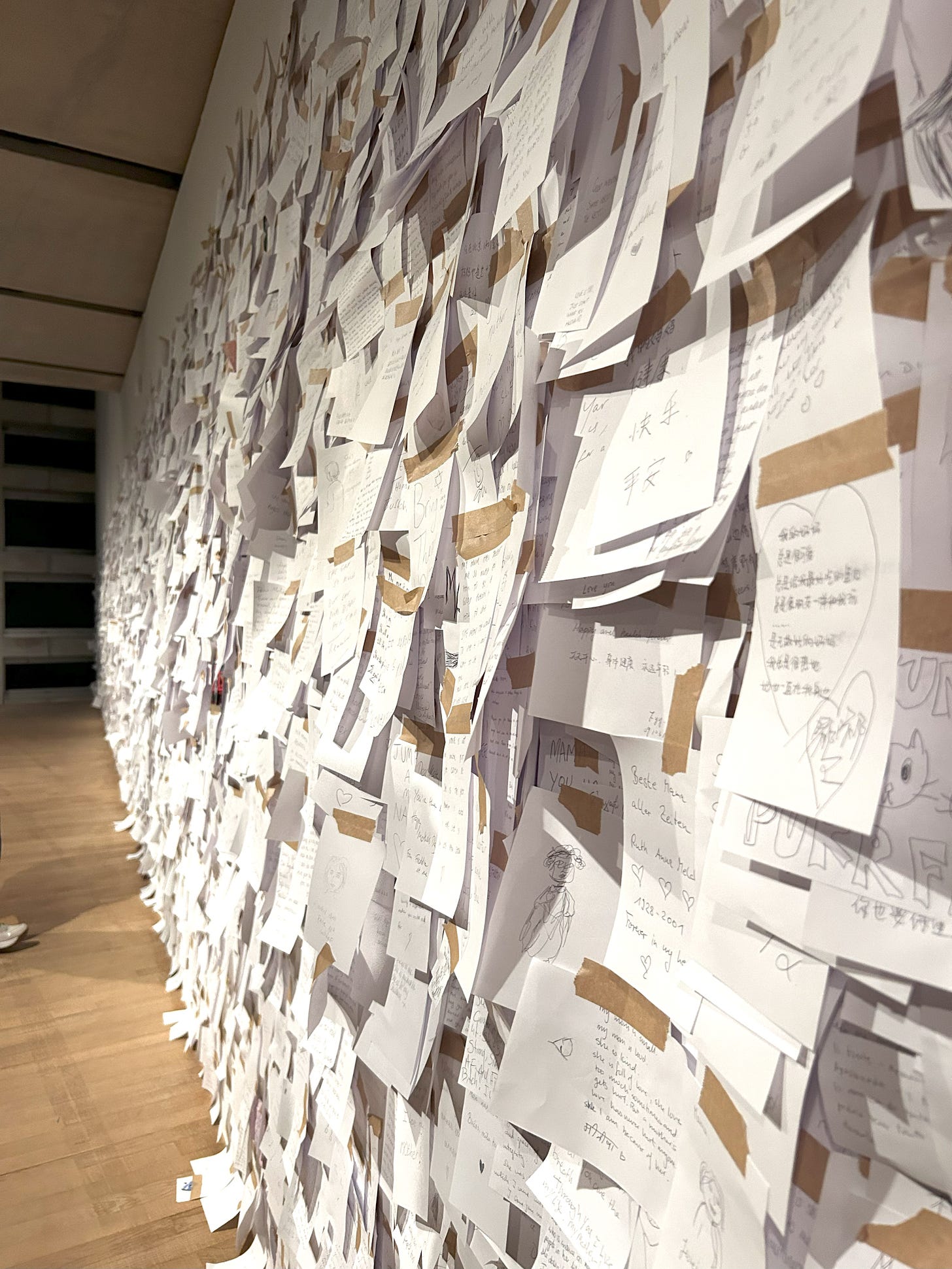 a wall of white papers with writing stuck on with brown tape