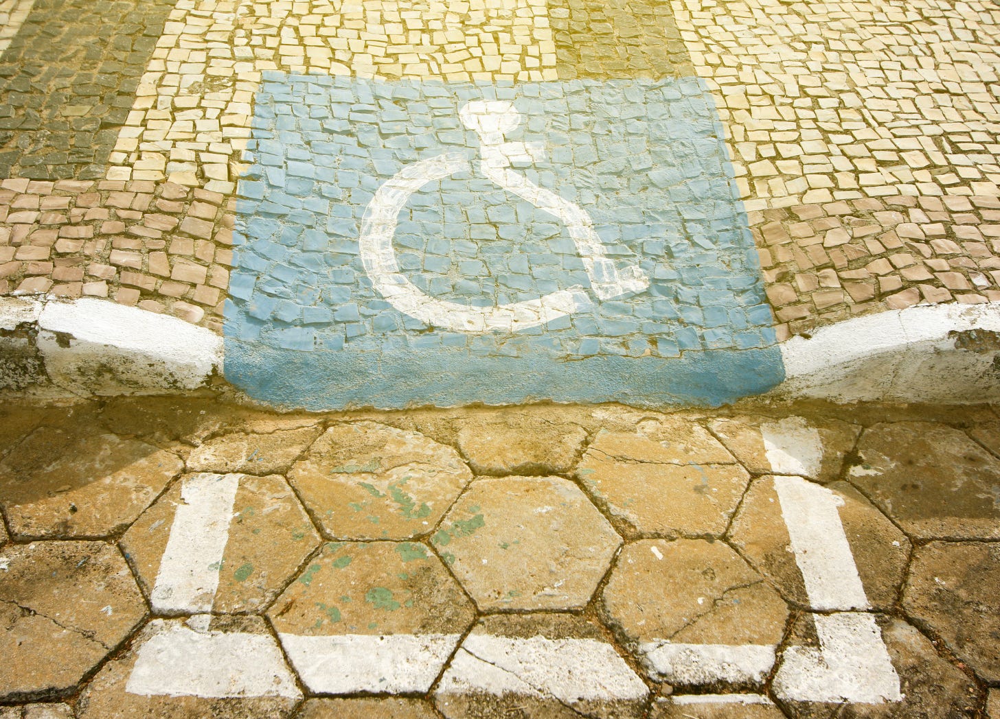 Wheelchair symbol sloppily painted onto a rough curb cut