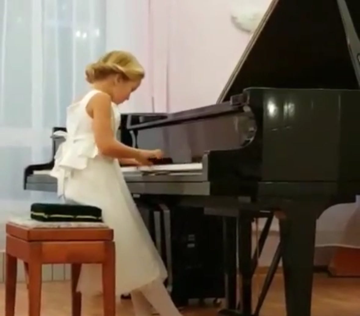 A9 year old girl, in white formal dress, is playing classical music on the baby grand piano.