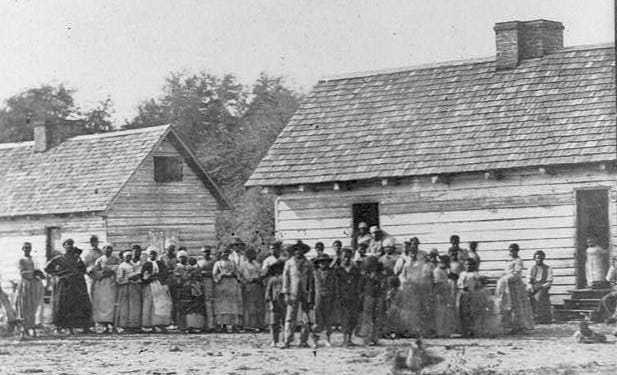 An undated photograph showing a large group of enslaved persons standing in front of plantation buildings in Beaufort, SC.