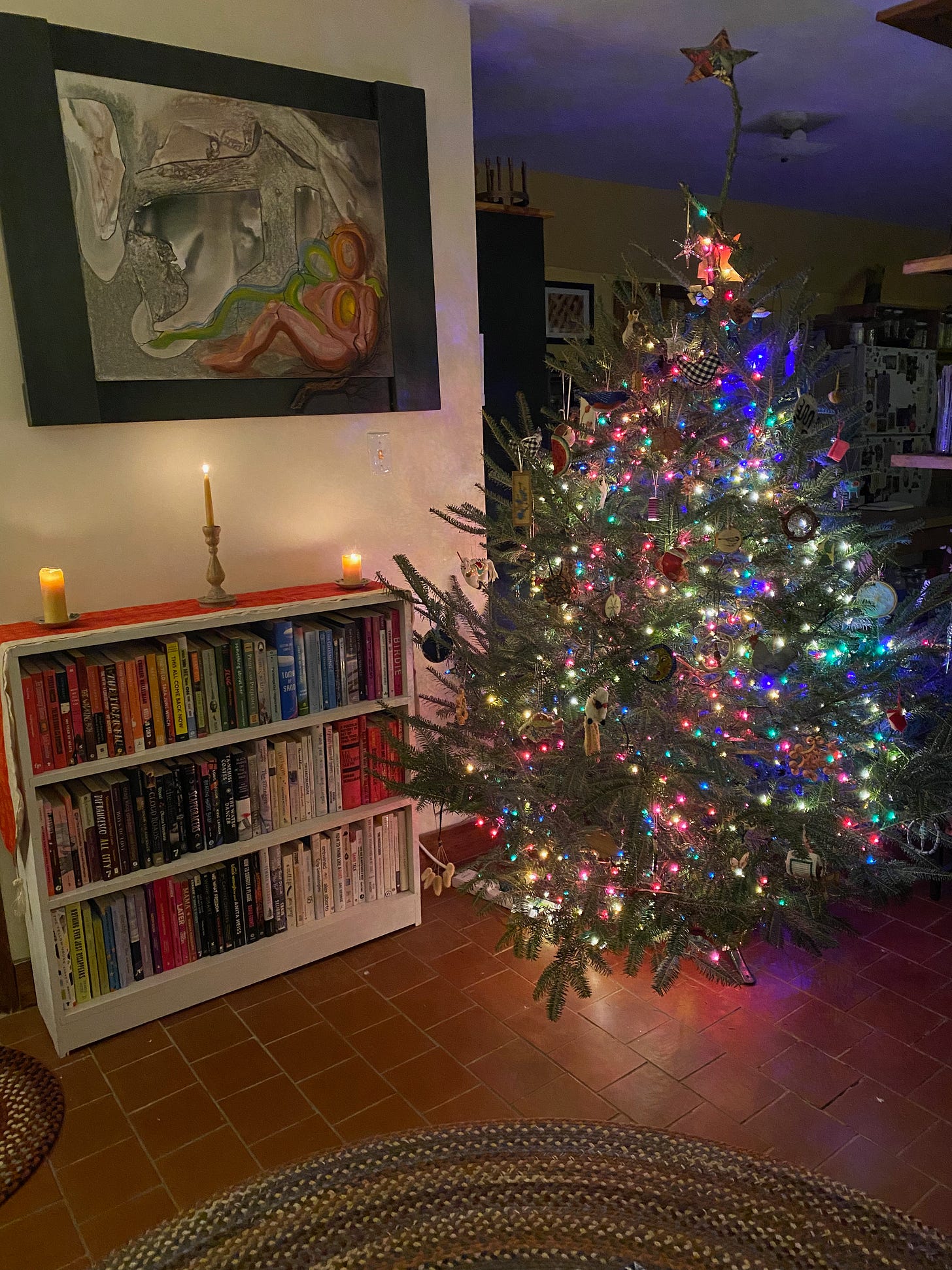 A lit up Christmas tree in my dark living room next to several candles on a bookshelf.