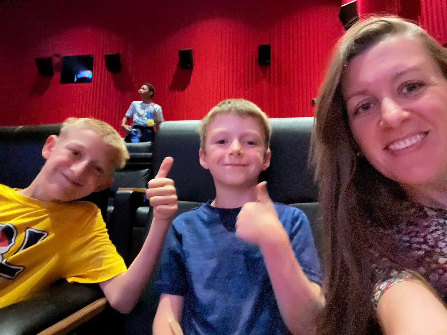 Amy's sons give a thumbs-up with smiles as Amy takes the group selfie in the movie theater