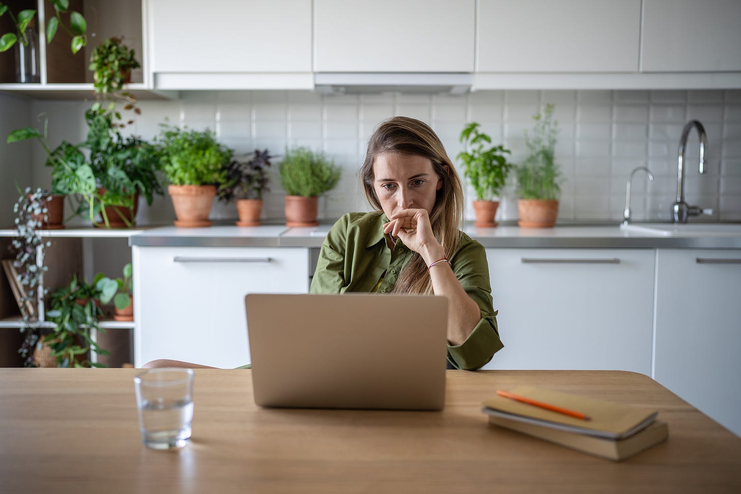 A stressed woman stares at her laptop screen while sitting in her kitchen.