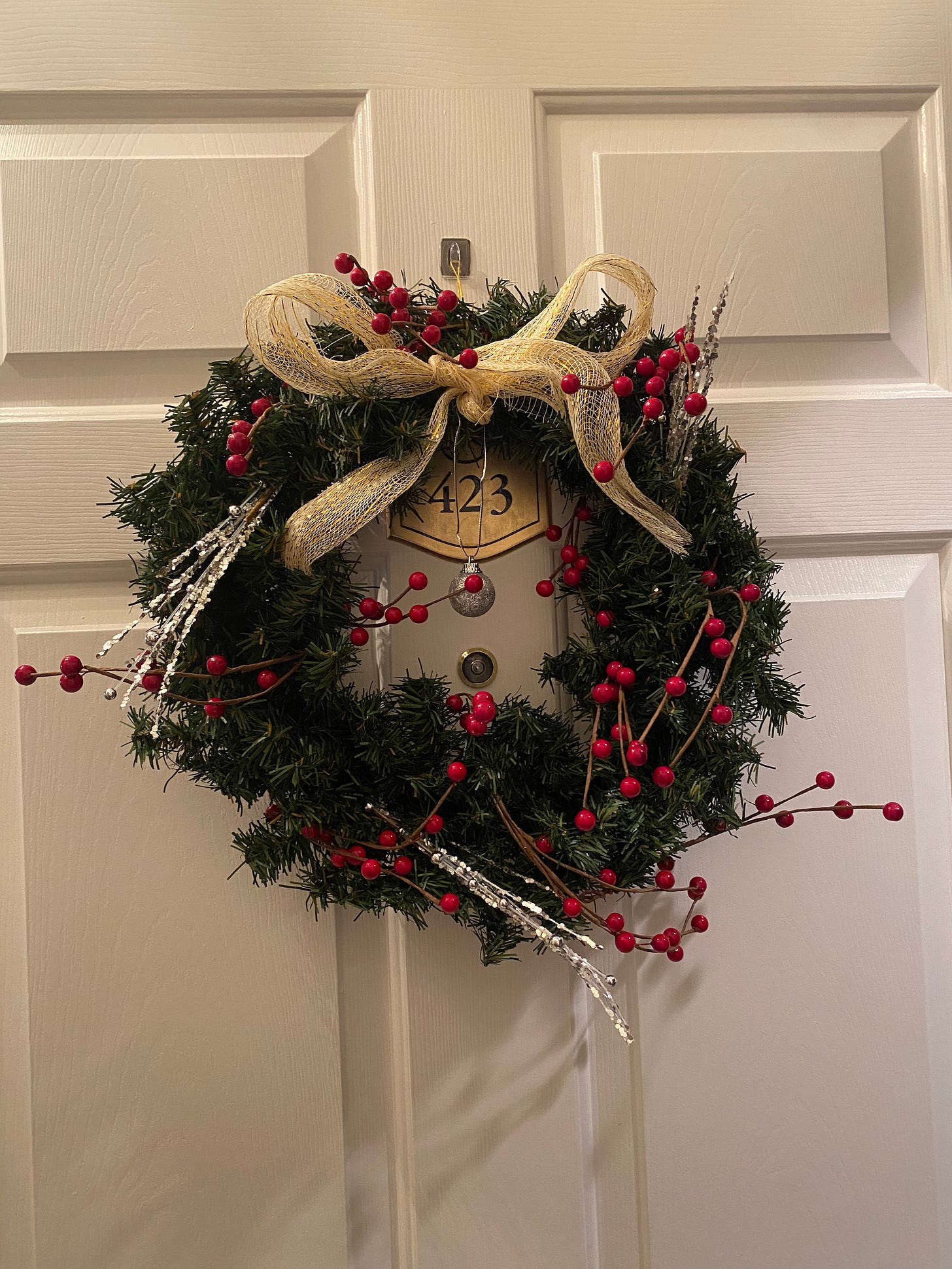 A door with a (fake) evergreen wreath on it. It's got red berries and silver picks in it, and a gold mesh bow tied at the top with a small silver ball dangling in the centre.