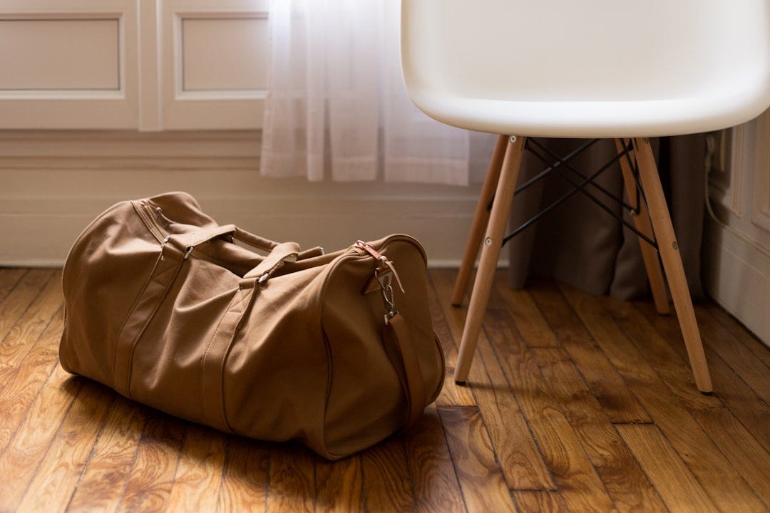 brown duffel bag beside white and brown wooden chair brown duffel bag beside white and brown wooden chair