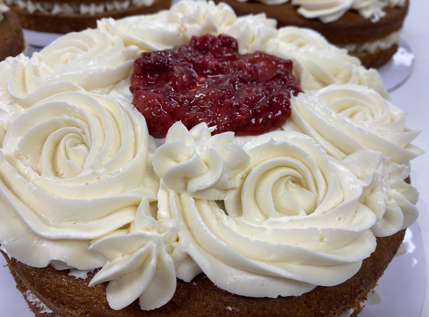 a layered vanilla cake with roasted strawberries on top and piped meringue flowers around the edge