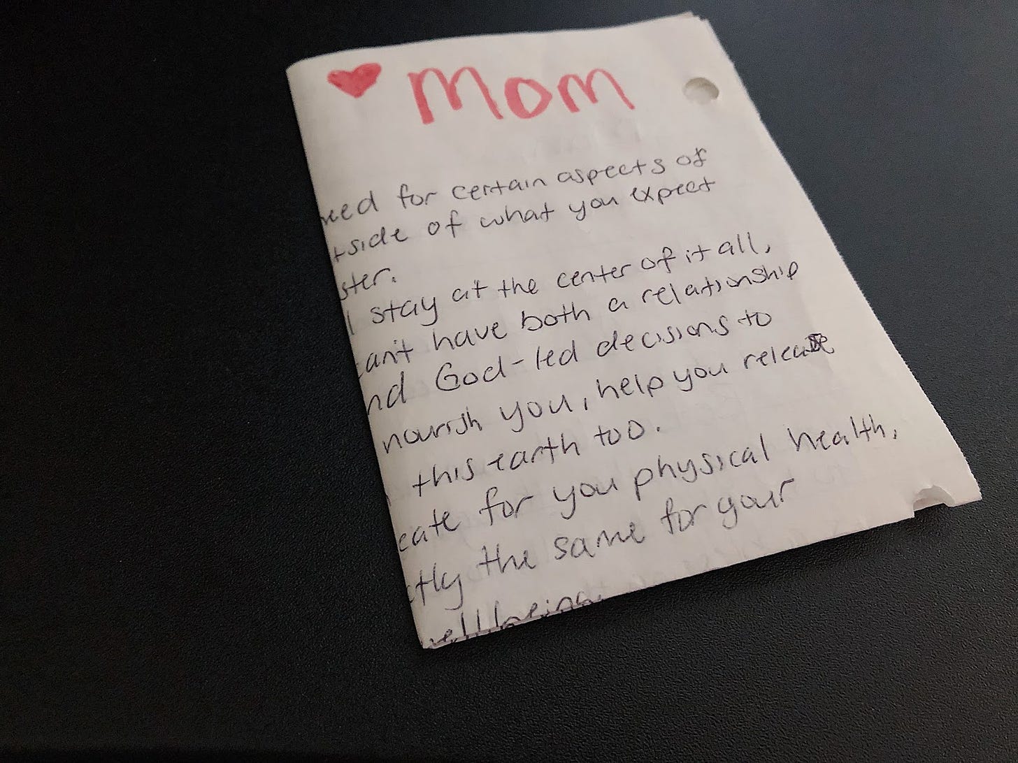 A folded up letter with "mom" and a heard drawn and written in read, placed on a black table.