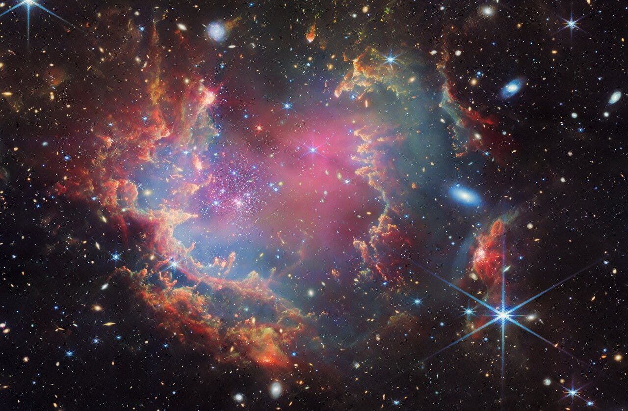 A colourful array of white and bluw stars sits surrounded by clouds of pink and brown gas against the black of deep space. 