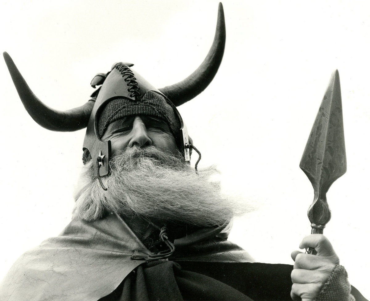 Moondog in his viking helmet, holding a spear. He has a long white beard and is wearing a cloak.