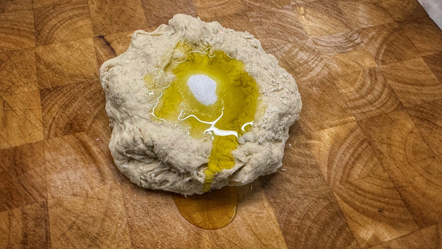 A dough ball on a cutting board with salt and olive oil put on top, waiting to be incorporated