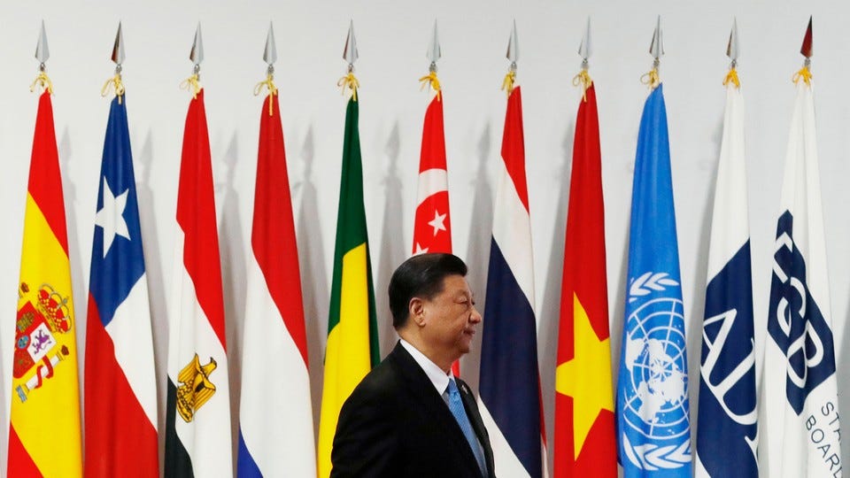 Xi Jinping stands in profile in front of international flags at a meeting of the G20 in 2019.