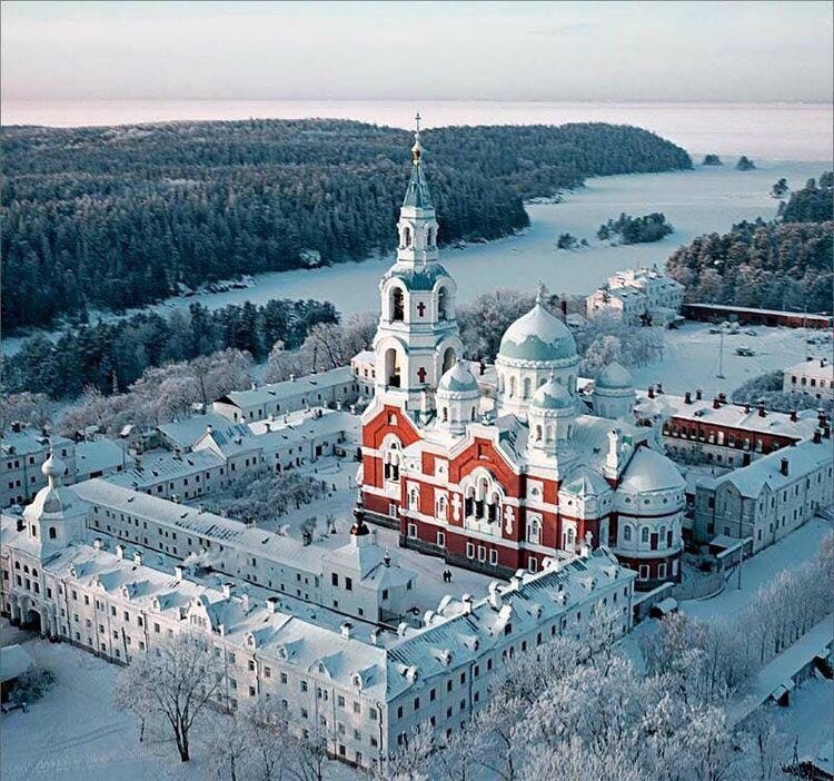 Photo of an island in wintertime, featuring a large monastery in the center surrounded by pine trees and ice