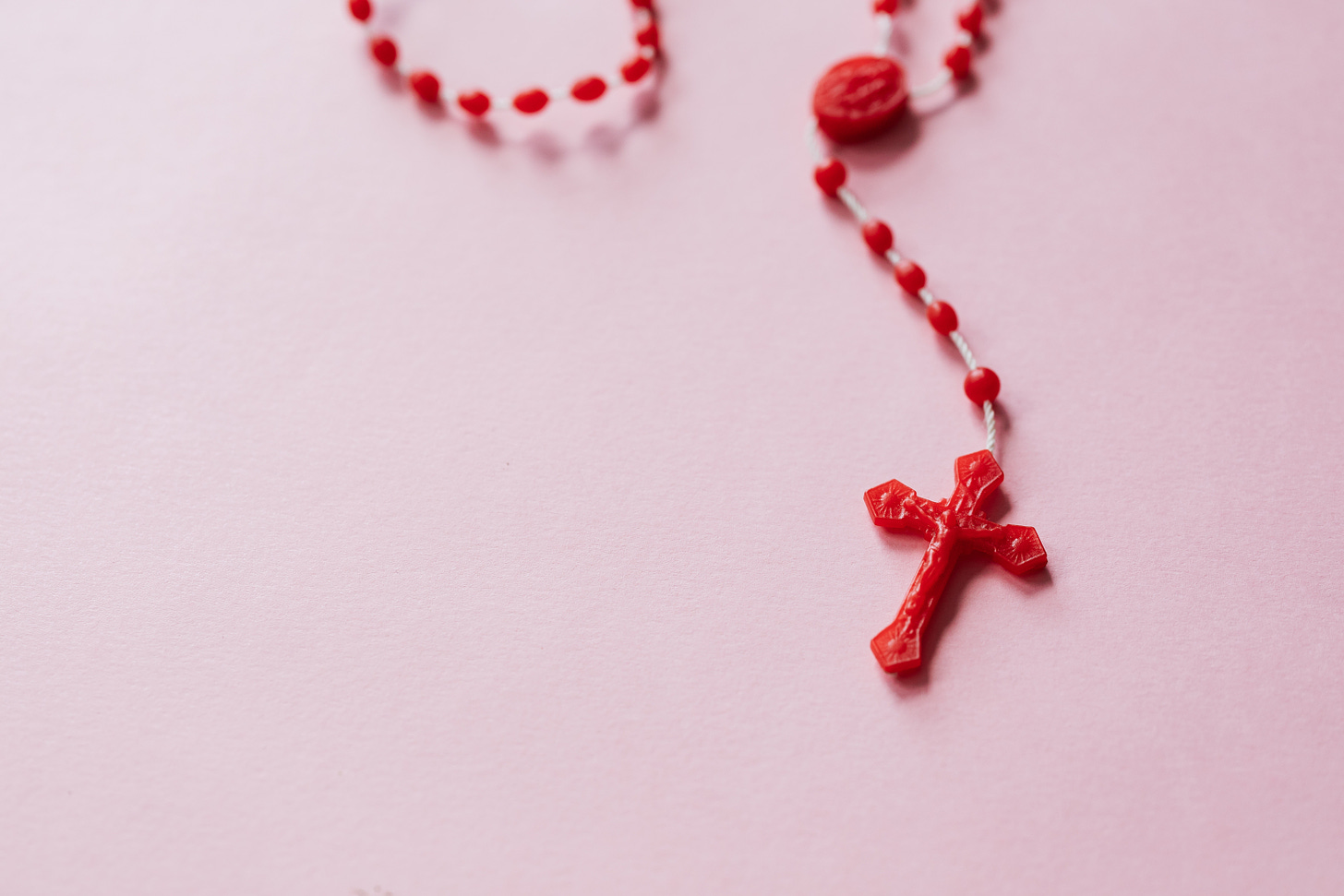 Red Plastic Rosary Beads on a pink background