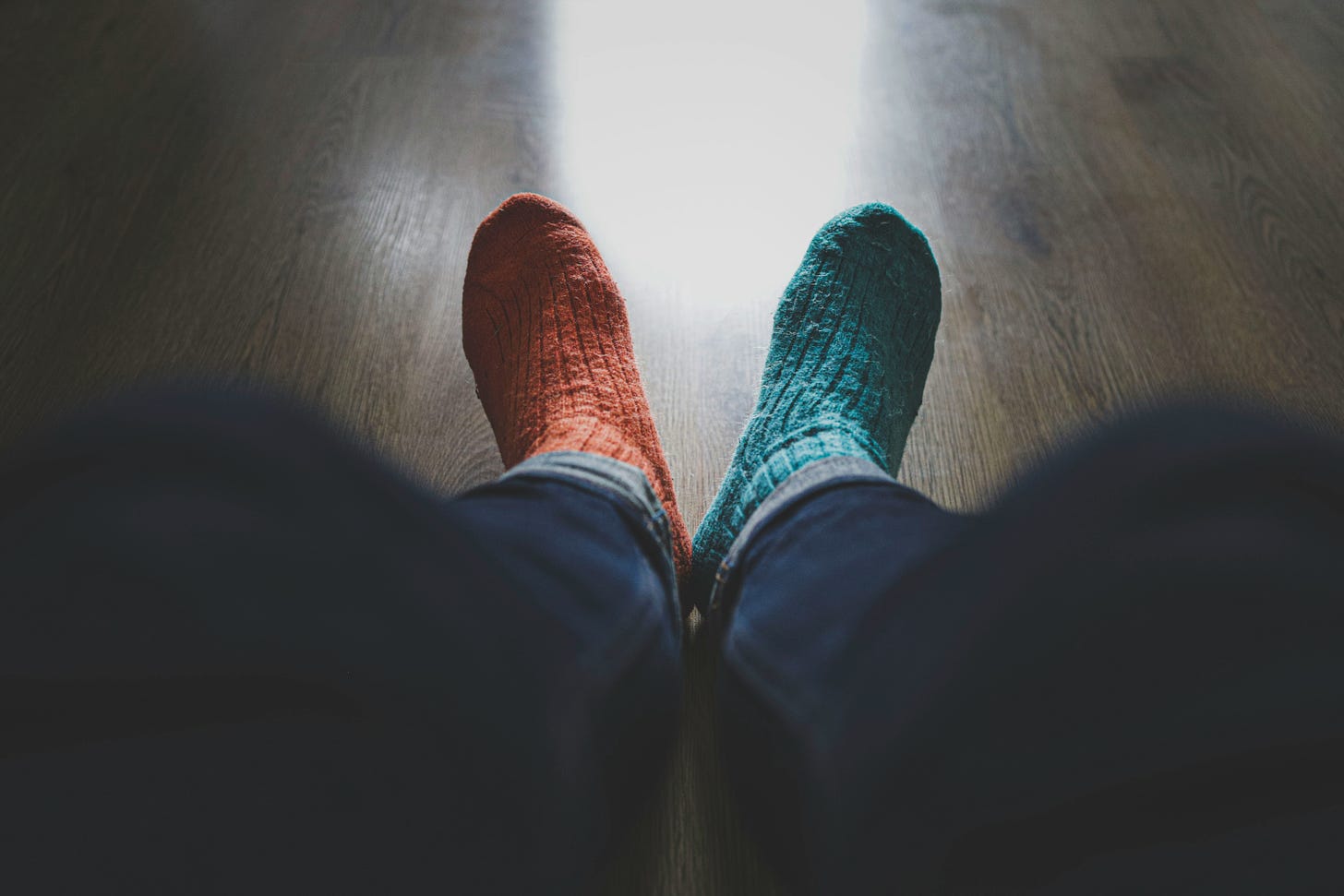 wearing long blue jeans, a person sits with two thick woolen socks - one red, one green