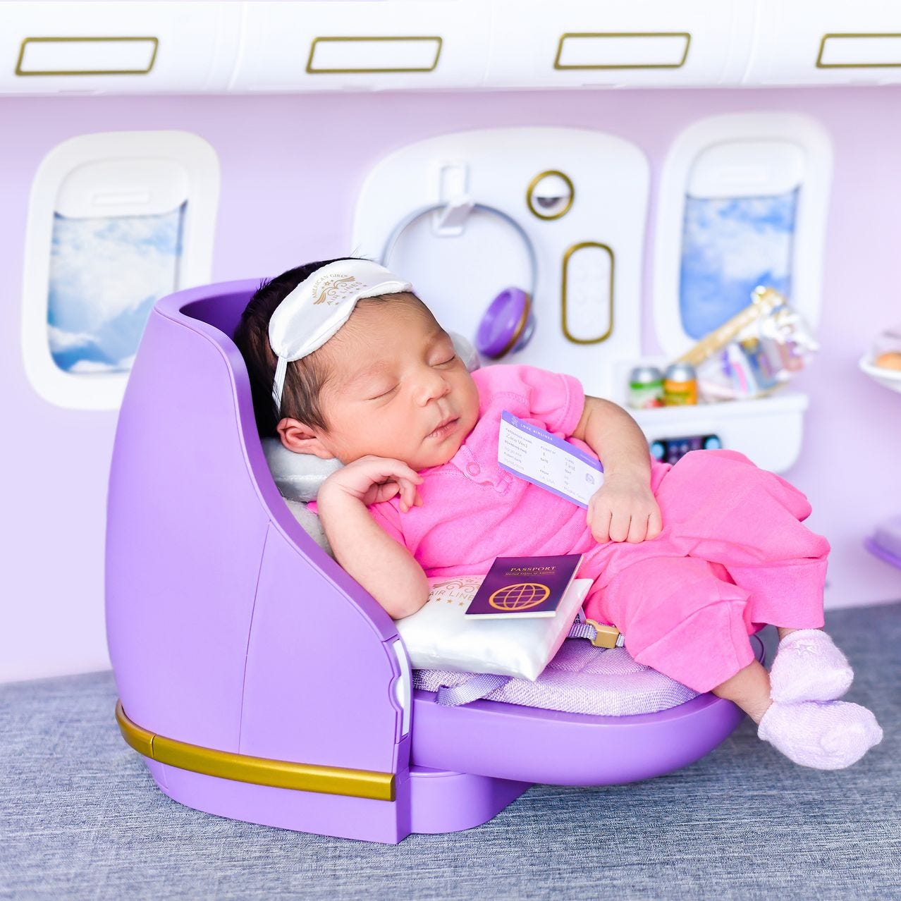 A baby sleeps in a miniature first-class airline cabin for her picture, wearing a sleep mask and clutching a ticket to Spain.
