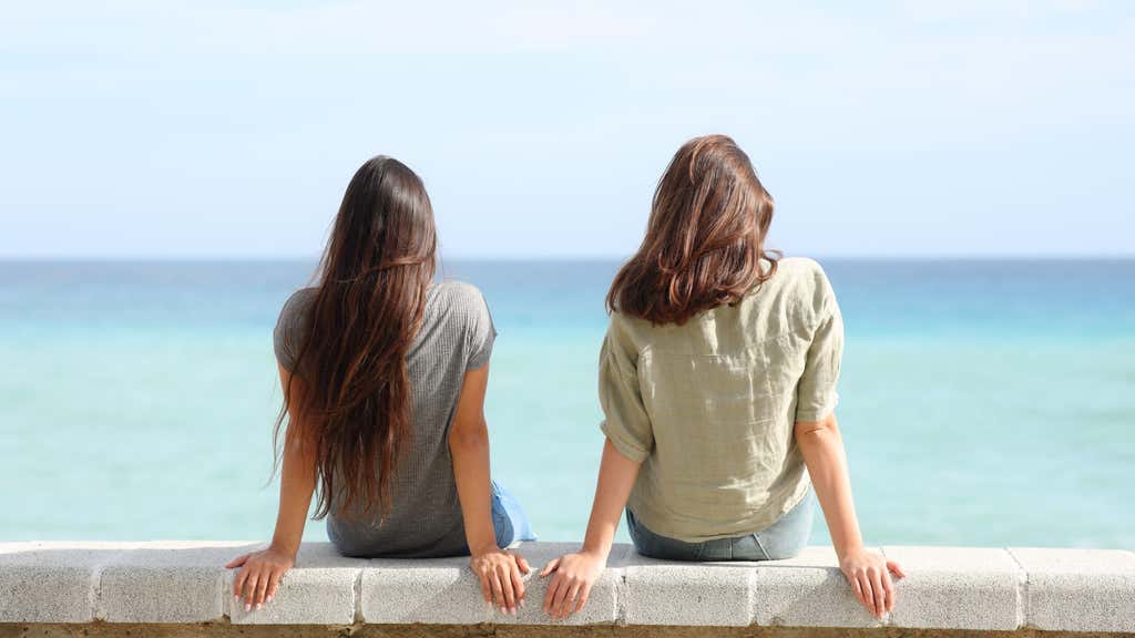 Two women sitting on a wall looking out to sea