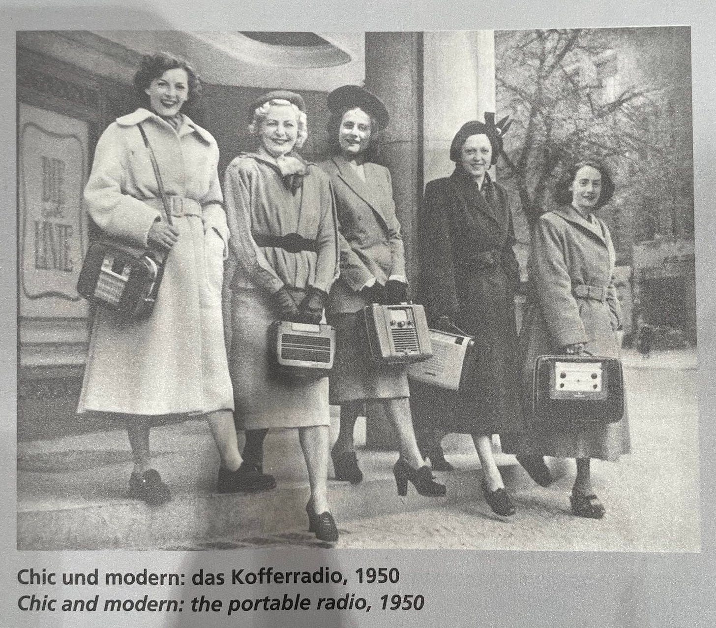 black and white photo of women in hats and overcoats carrying portable radios. captioned: chic und modern: das Kofferradio, 1950 (Chic and modern: the portable radio, 1950)