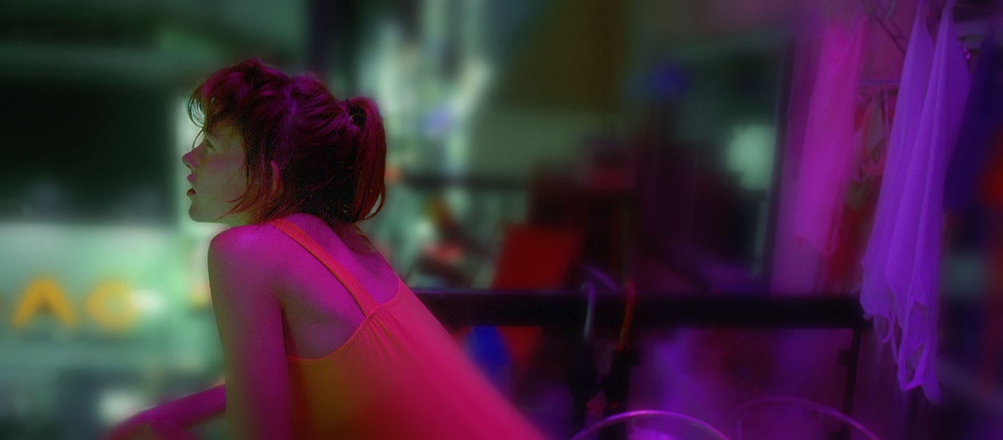 Movie still from Enter the Void. A woman gazes out on a balcony at night in Tokyo, drenched in neon.