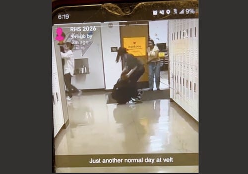 A person is seen laying on the linoleum hallway of a school while another person stands over them while grabbing them. Neither persons' face is visible because their hair is blocking them.