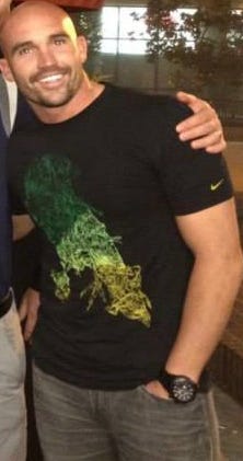 A bald white man in a black T-shirt with a Nike logo on the sleeve, hand in his pocket, with a watch.
