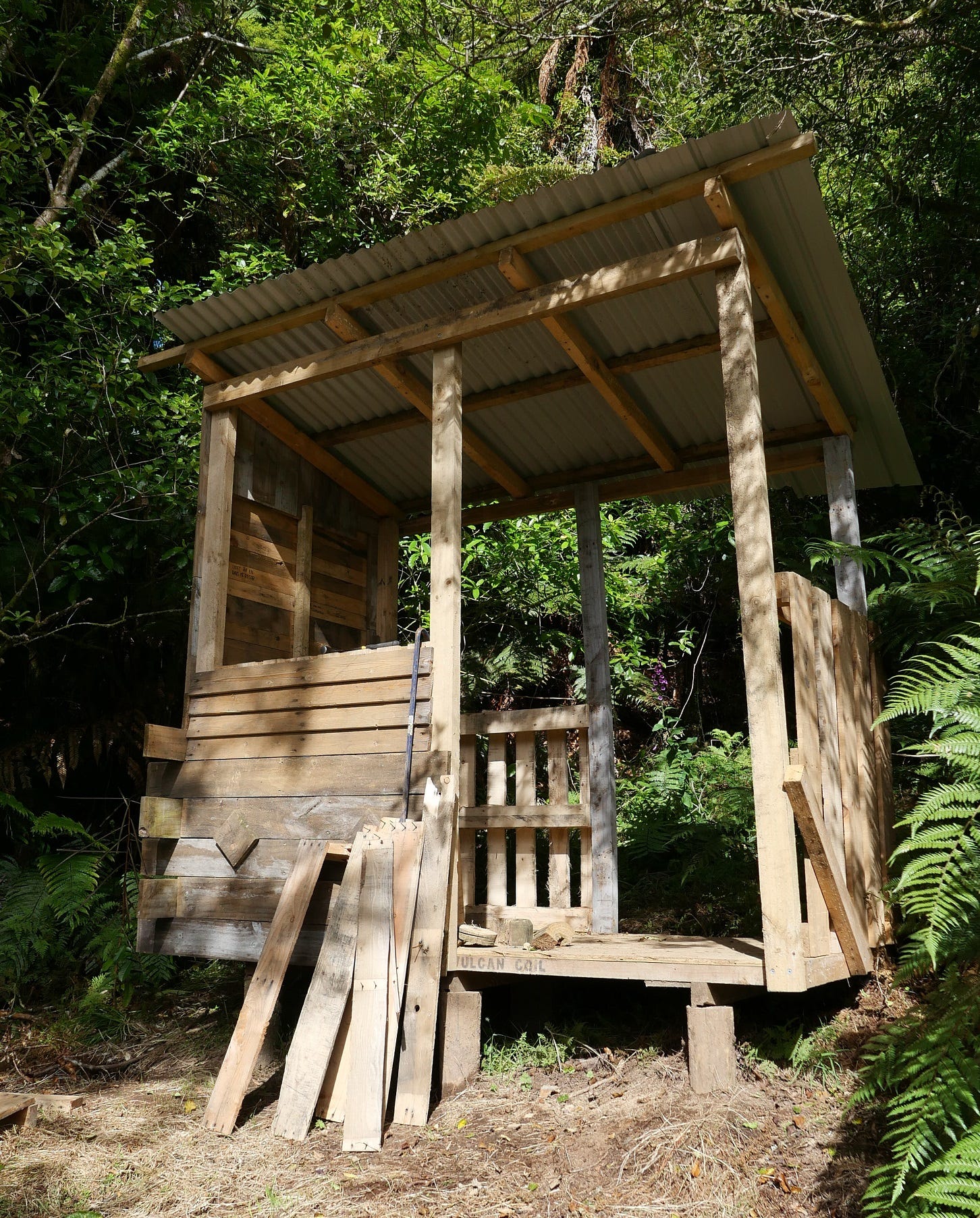 A platform with corrugated roof, one complete wooden wall and other partial walls.