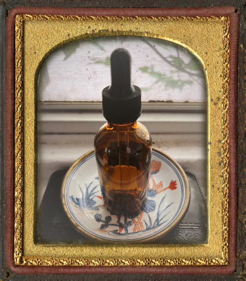 framed photograph of a small brown apothecary bottle with a black stopper resting on a colorful dish by a window.