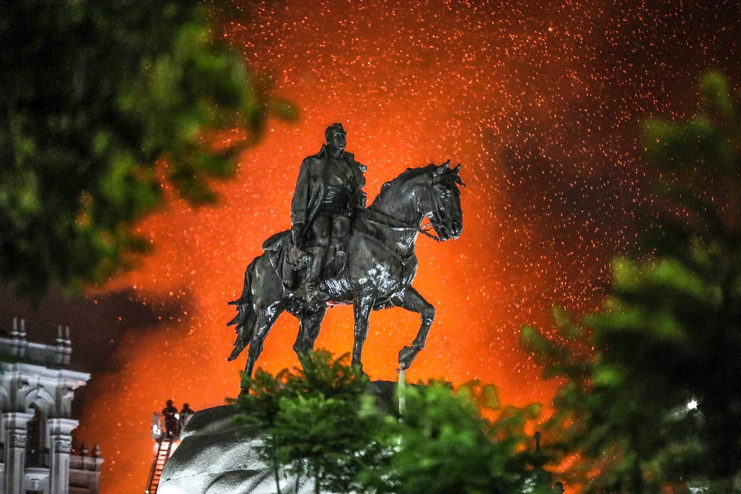 a fire erupts behind a statue of a man on a horse