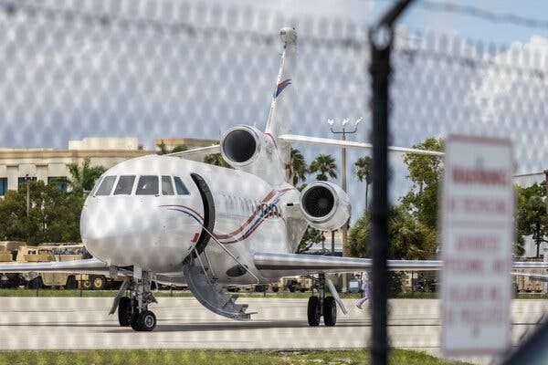 A small plane sitting on the tarmac with its stairway extended, viewed through a fence.