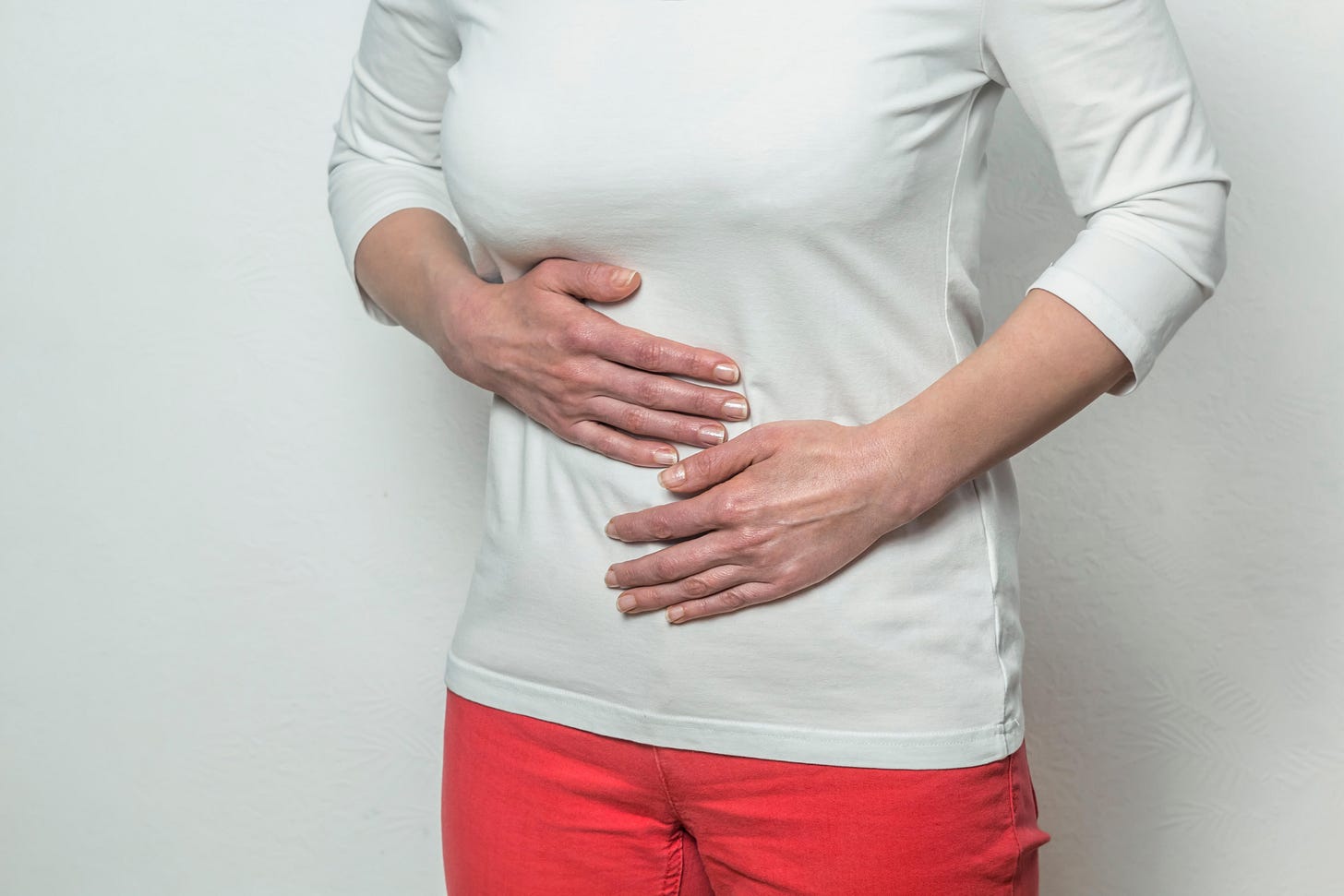 A woman, who is wearing a white top and red shorts, putting her hands on her belly