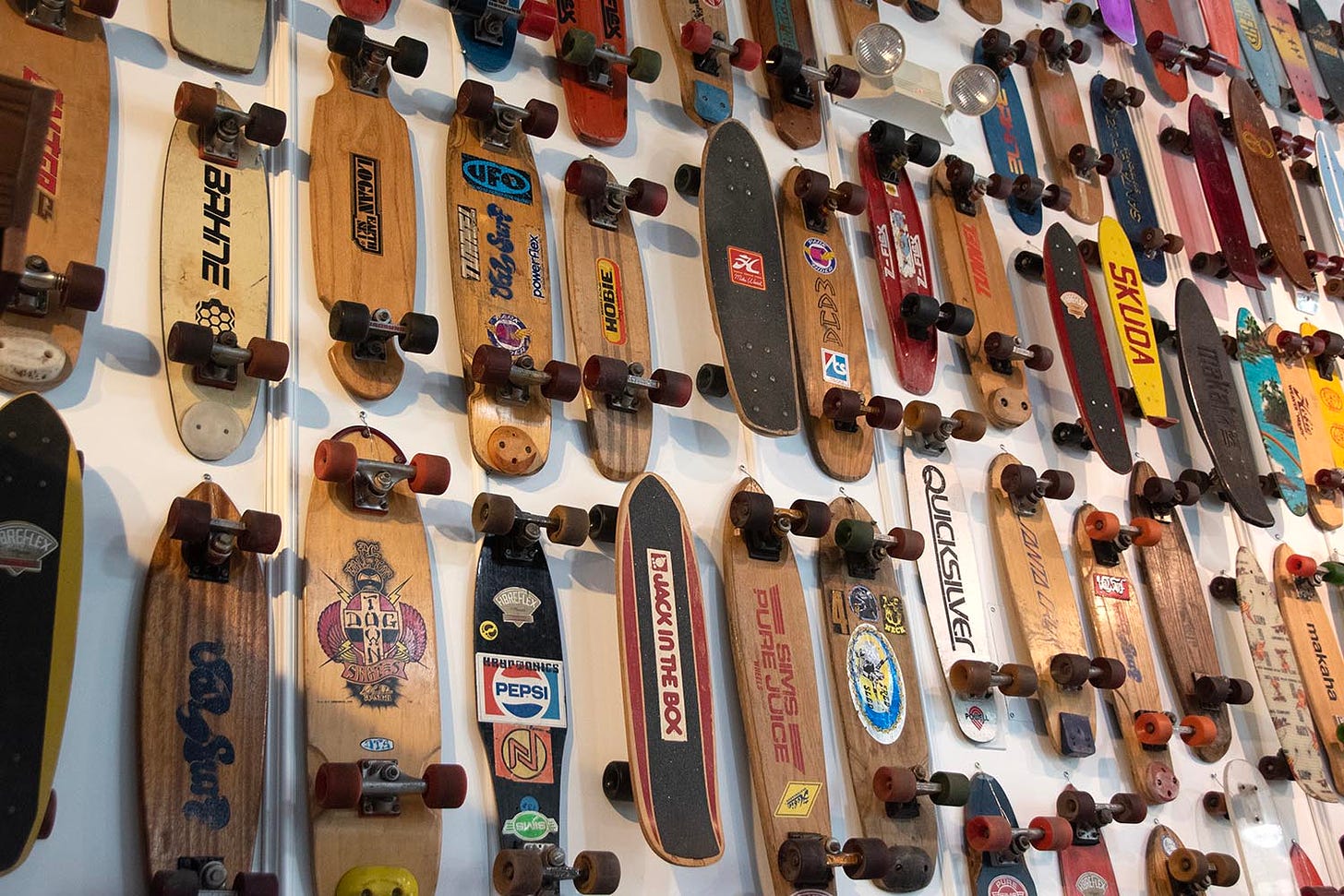 A medium-distance shot of a spread of 70s skateboards at Skateboard Hall of Fame. The image shows around 60 boards–overflowing the frame of the image–on a wall that is at least 20 feet high.