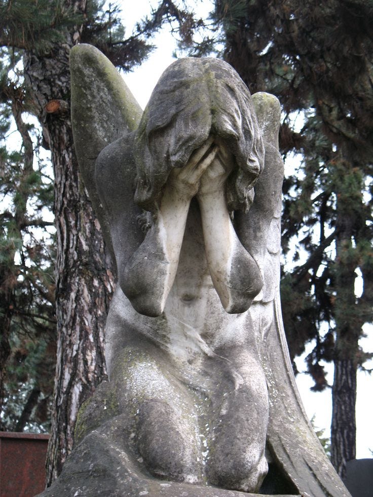 This may contain: an angel statue sitting next to a tree with its hands on it's face