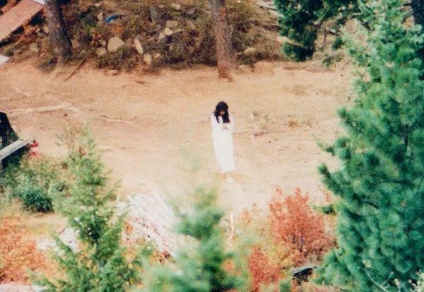 Photo shows Vicki Weaver standing in the woods wearing a long, white dress.