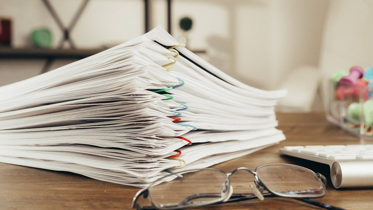 Free Close-up of a stack of office papers on a desk with glasses, emphasizing organization. Stock Photo