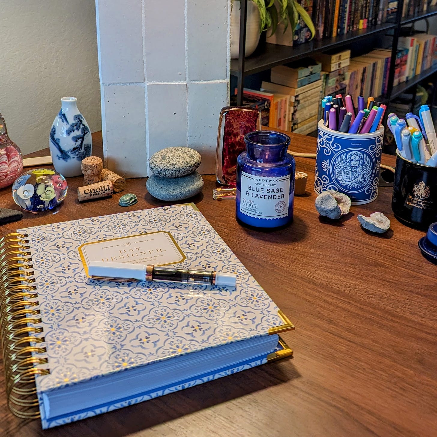 Desktop with planner, candle, stones, paperweights, and two cups full of pens and highlighters