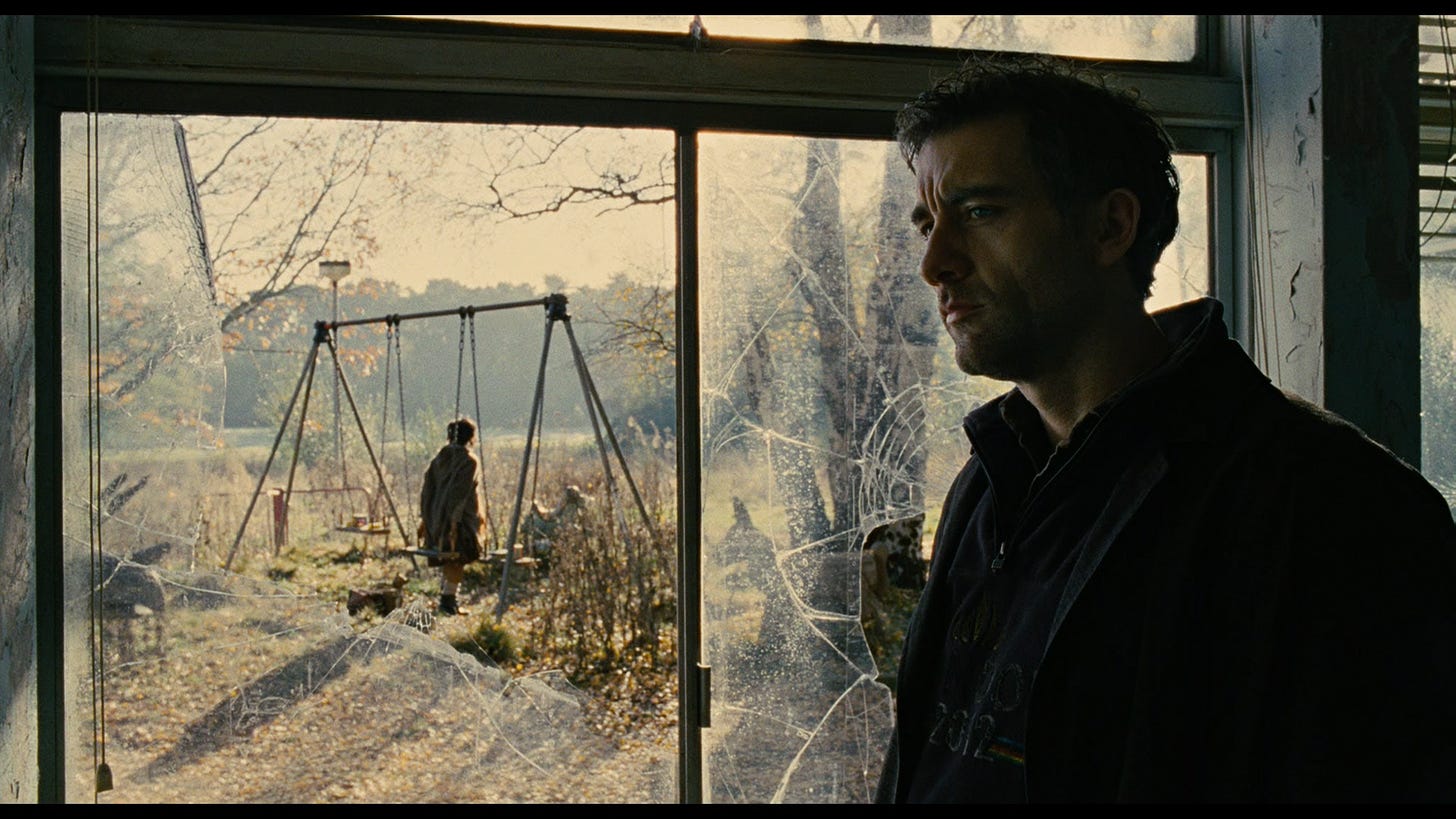 Clive owen watches from a cracked window inside an abandoned school as a young woman stands near a swingset