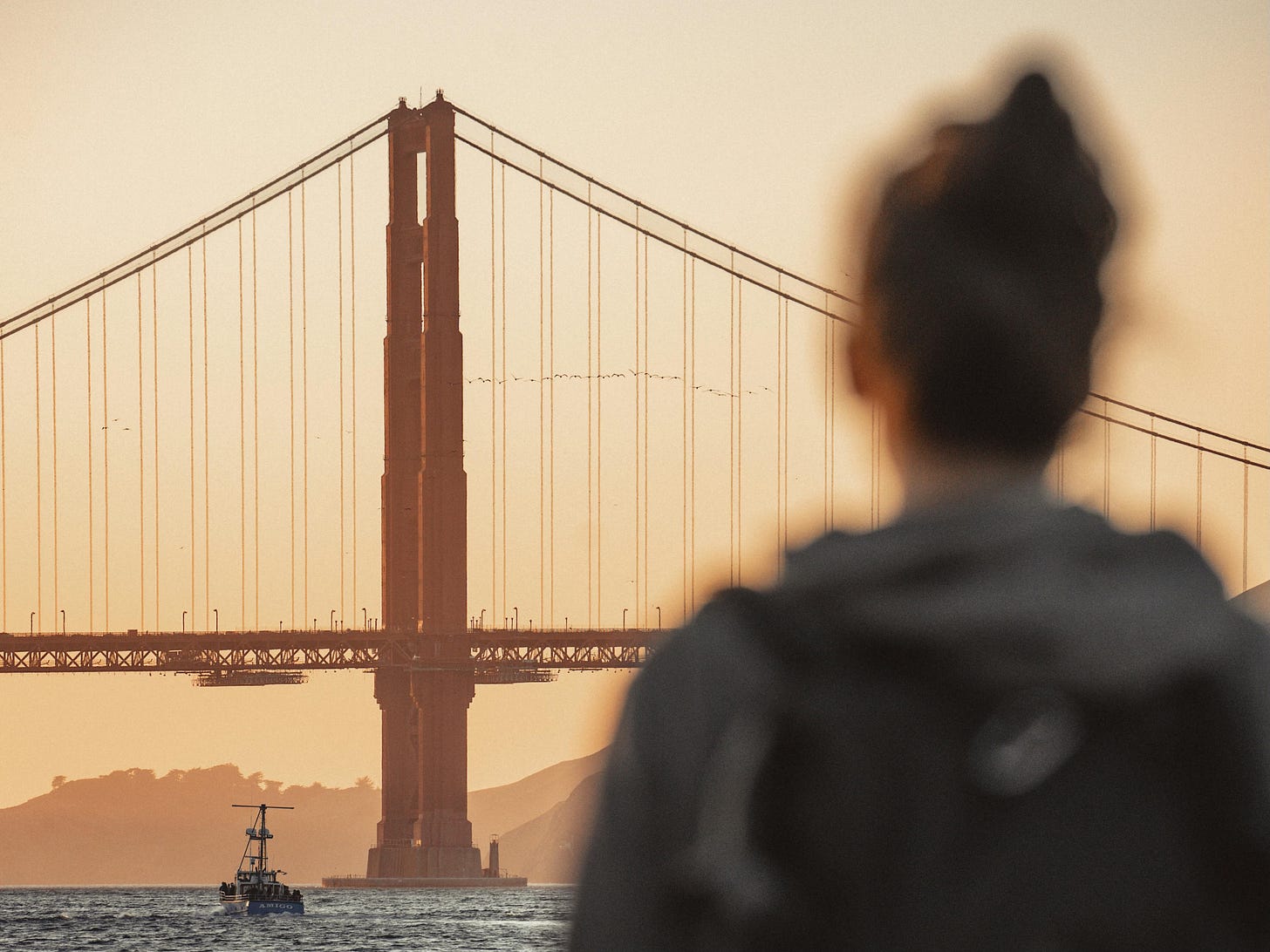 Photo of the back of a woman gazing at the Golden Gate Bridge in San Francisco on a hazy morning.