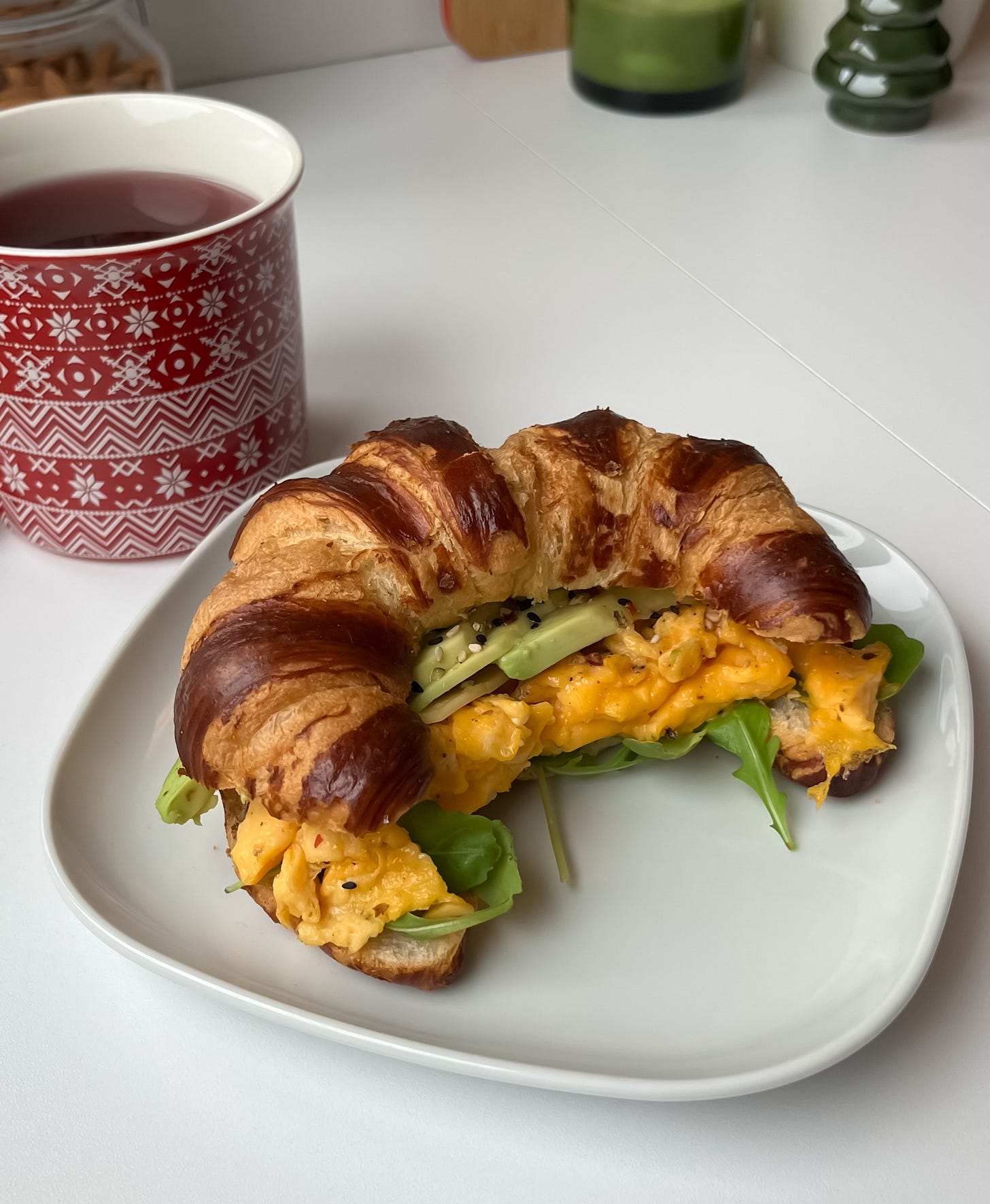 Healthy breakfast croissant with eggs, cheese, avocado, and arugula, served on a wooden plate for a quick, balanced meal.