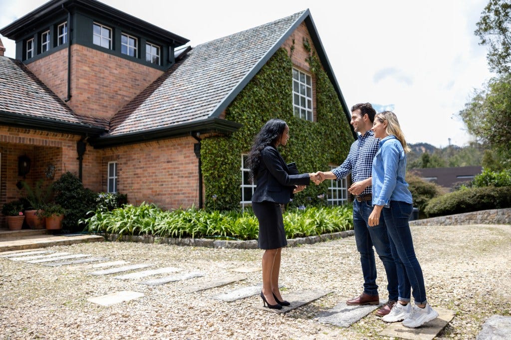 Real estate agent happily greeting a couple with a handshake at a house showing