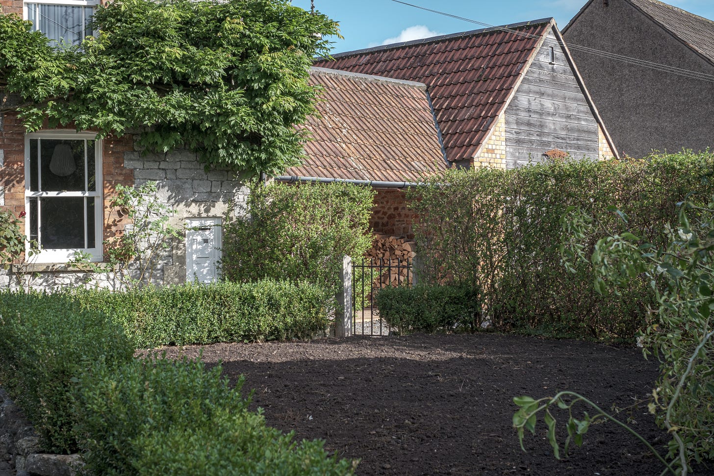 Bare soil front garden with box hedges and old postbox in stone cottage