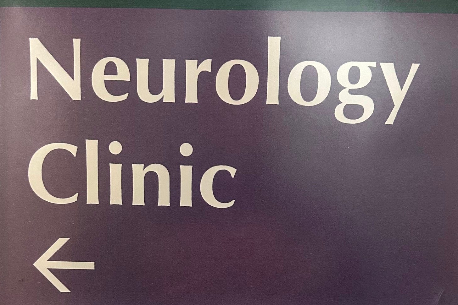 A brown sign with white lettering with the words "Neurology Clinic" and an arrow pointing to the left.