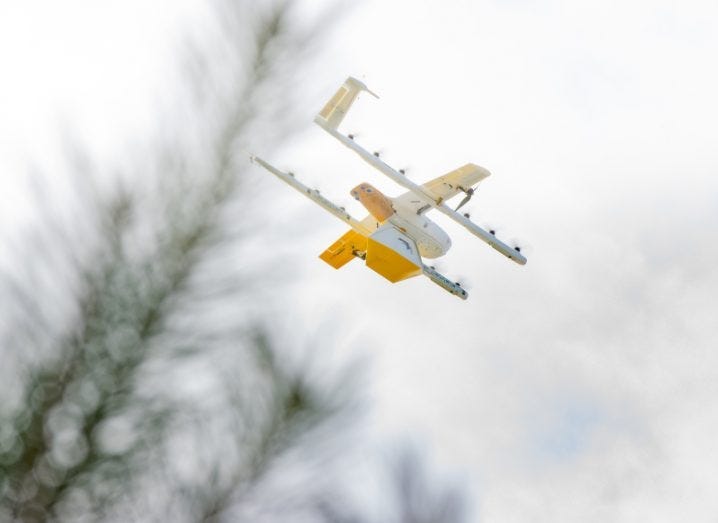 A Wing delivery drone mid-air holding a package.