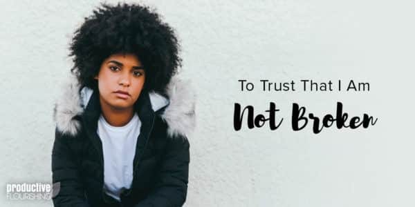 Black woman in a jacket sitting against a white wall. Text overlay: To Trust That I Am Not Broken