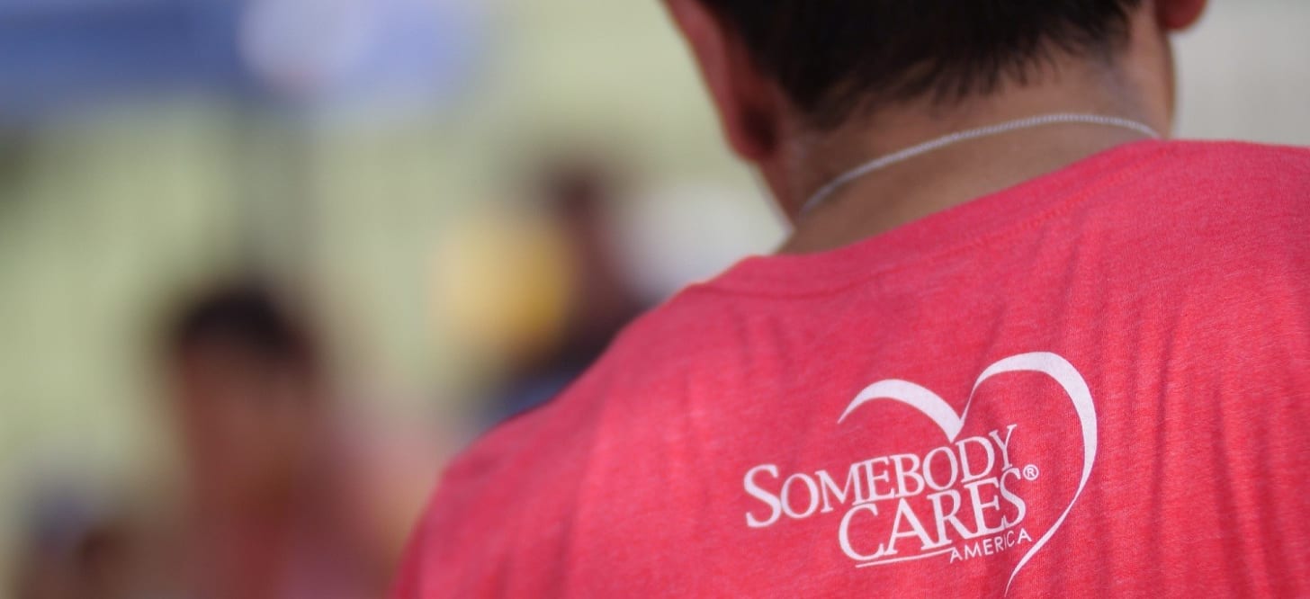 Image of the back of a man with a Somebody Cares America logo on the back of his tshirt.