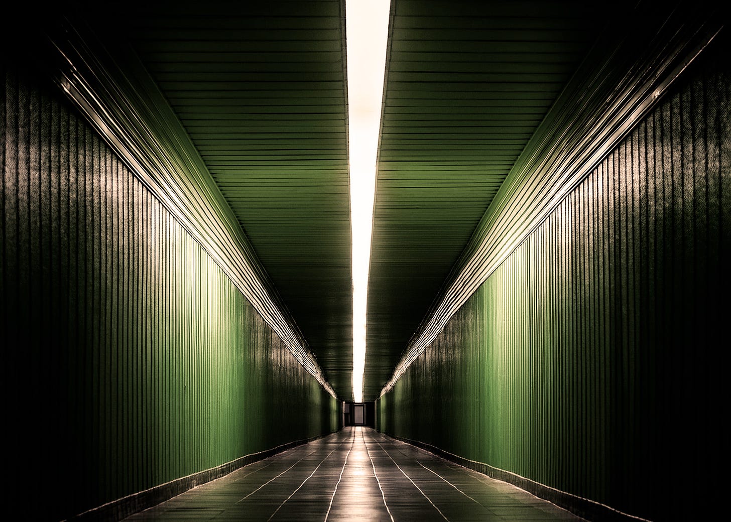 surreal dark hallway with no doors, green walls and black tiled floor, illuminated by a single thin strip of white light running the length of the ceiling